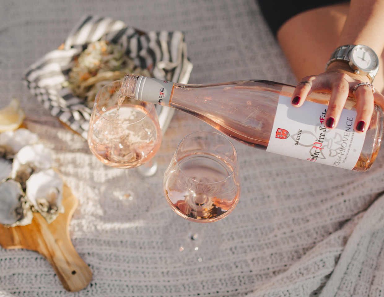 Woman pouring a glass of Bieler Pere & Fils Sabine Rose outside with a picnic of oysters.